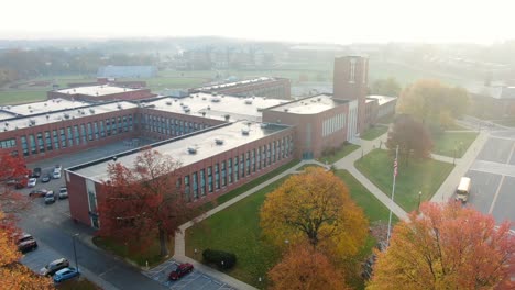 High-angle-aerial-of-school-bus-leaving-large-public-school-on-foggy-morning