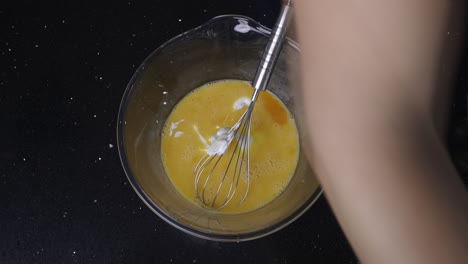 Topdown-view-of-whisking-yogurt-into-a-bowl-of-liquid-eggs