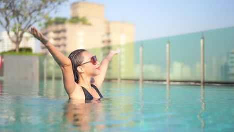 Woman-in-rooftop-pool-raising-hands-with-joy-on-face