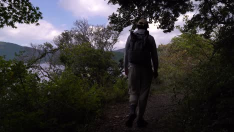 Excursionista-Masculino-Caminando-Por-El-Bosque-Verde-Junto-Al-Hermoso-Lago-Y-El-Cielo-Azul