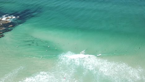 Drone-aerial-over-beautiful-blue-water-with-a-group-of-surfers-catching-waves