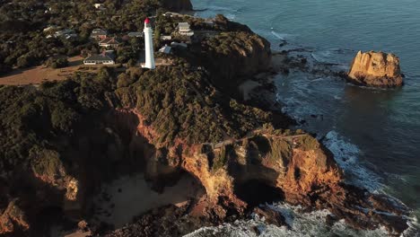 Drone-aerial-of-aireys-inlet-lighthouse-by-the-ocean-pan-up-during-sunset-on-The-Great-Ocean-Road