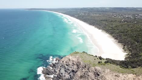 Drone-aerial-pan-down-to-beautiful-blue-beach-with-waves-and-white-sand-near-cliff-side