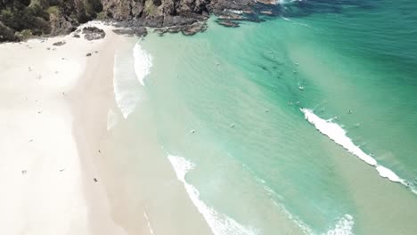 Drone-aerial-panning-down-to-see-surfers-catching-waves-at-a-beautiful-blue-water-beach