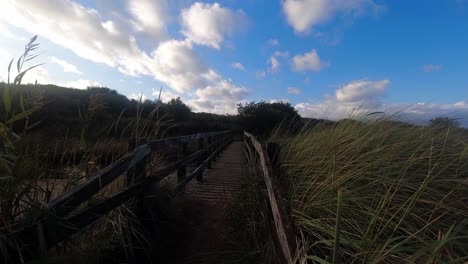 Zeitraffer-Dolly-Strandsteg-Aus-Holz-Mit-Langem-Gras-Und-Vorbeiziehenden-Wolken