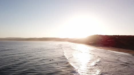 Drohnenantenne-Bei-Sonnenuntergang-Am-Strand-Mit-Surfern,-Die-Wellen-Fangen