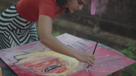 Medium-slow-motion-shot-of-beautiful-young-talented-artist-works-on-an-abstract-artwork-while-she-draws-lines-with-the-brush-with-white-paint-in-garden
