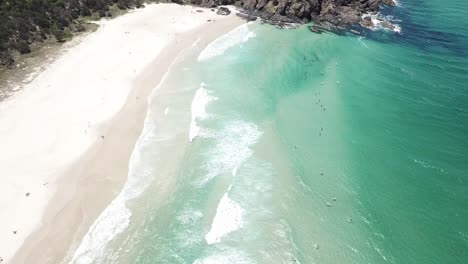 Drone-aerial-with-slow-pan-up-with-surfers-in-a-blue-clean-beachy-ocean