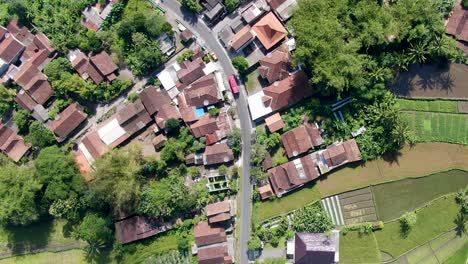 Red-bus-driving-through-small-Indonesia-town,-aerial-top-down-view