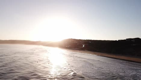 Drone-aerial-during-sunset-at-beach-with-surfers-bouncing-on-waves