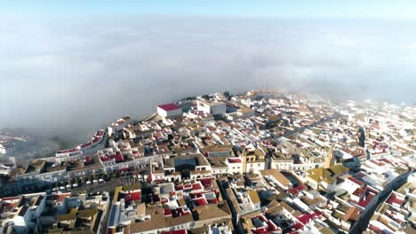 Langsamer-Kamerafahrt-Nach-Hinten-über-Die-Altstadt-Medina-Sidonia-In-Spanien-Mit-Blick-Auf-Die-Gesamte-Altstadt-Mit-Weißen-Gebäuden-Mit-Vereinzelten-Roten-Dächern-Und-Den-Wolken-Im-Hintergrund