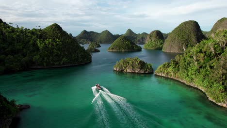Small-boat-drives-through-in-Raja-Ampat-Indonesia,-in-between-tropical-islands,-turquoise-waters,-and-coral-reefs