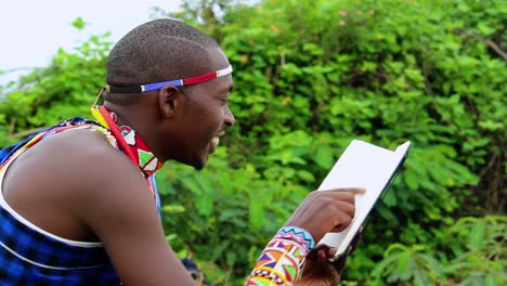 Happy-Masai-man,-sitting-in-a-forest,-reading-a-book,-in-Africa