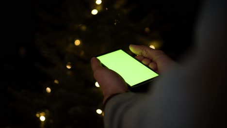 Holding-Smartphone-with-greenscreen-in-front-of-christmas-tree