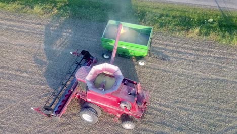 Aerial-drone-pan-around-of-a-red-combine-unloading-soybeans-into-a-green-wagon-about-an-hour-before-sundown