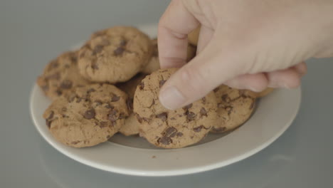 Hand-placing-chocolate-chip-cookies-on-a-white-plate---high-angle