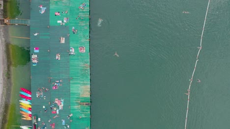 Birds-Eye-Aerial-View,-Pontoon-at-Lakefront-of-Perucac-Lake-Serbia,-People-Enjoying-in-Water-and-Sun-on-Summer-Day