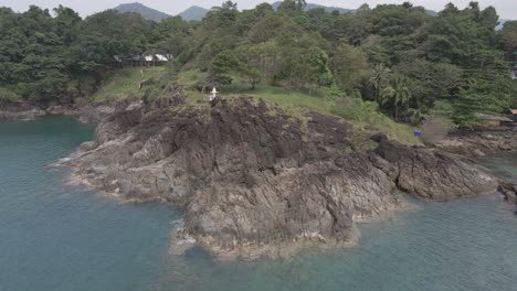Drone-right-orbit-shot-,-birds-eye-view-of-granite-rock-coastline-on-a-tropical-Island-with-jungle-lush-green-forest-and-ocean