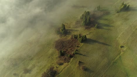 Stunning-green-hill-slowly-being-covered-by-light-mist-in-Poland,-aerial