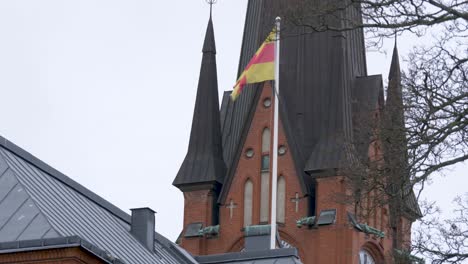 Swedish-national-church-flag-gently-waving-on-pole,-standing-near-Scandinavian-Building---Wide-shot