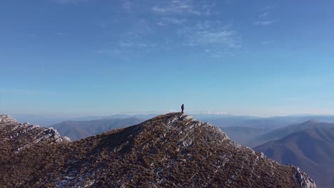 Person-stands-on-the-peak-of-a-rocky-mountain-drone-shot