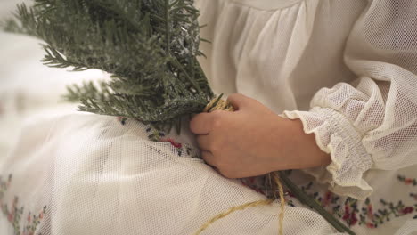 Slow-motion-shot-of-Young-girl-holding-Pine-Christmas-Ornament-Branch-in-white-festive-dress---Close-up