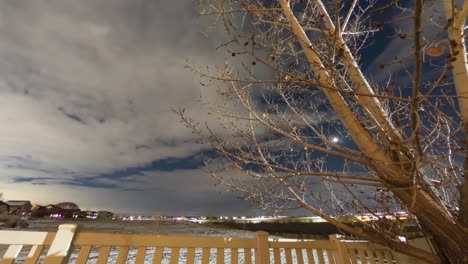 Night-time-time-lapse-of-clouds,-the-setting-moon,-rotating-stars-and-airplane-trails-in-the-winter-sky-above-an-urban-suburb