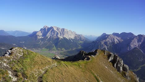 Dos-Excursionistas-Distantes-Alcanzan-La-Cruz-De-La-Cumbre-De-Una-Montaña-En-Los-Alpes