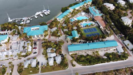 A-daytime-drone-shot-of-a-tropical-island-resort-with-tennis-courts,-waterways-and-boats-visible