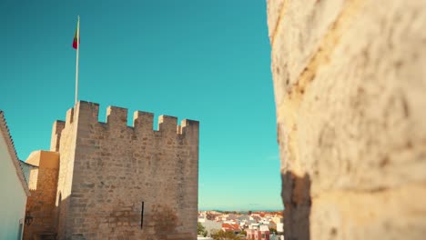 Portugal-Loule-stone-wall-reveal-castle-tower-battlements-with-flag-in-truck-camera-movement-under-blue-sky-4K