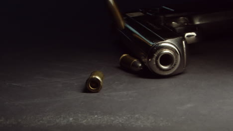 Bullets-drop-near-handgun-on-table-and-roll-away,-slow-motion