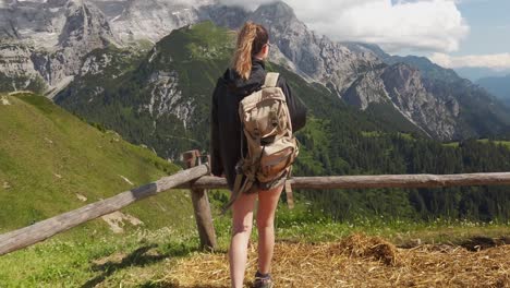 view-from-behind-of-a-hiker-tourist-traveler-woman-with-backpack-walking-n-enjoying-the-view-with-the-Dolomites-in-the-background