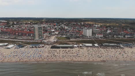 Aerial-footage-revealing-a-crowded-beach-along-a-North-Sea-city-shore-of-Zandoort,-Netherlands