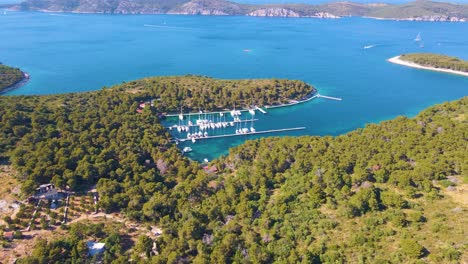 Yachten-Legen-In-Einer-Bucht-Nahe-Der-Küstenstadt-Kroatiens-An,-Vor-Dem-Hintergrund-Des-Blauen-Himmels-Und-Des-Blauen-Klaren-Wassers,-Grüner-üppiger-Bäume-Und-Häuser-Mit-Roten-Dächern