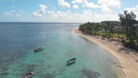 Aerial-4K-Establishing-shot-of-Clear-Blue-Water-along-beach-front-with-rowing-boats-and-palm-trees-in-Balaclava,-Mauritius