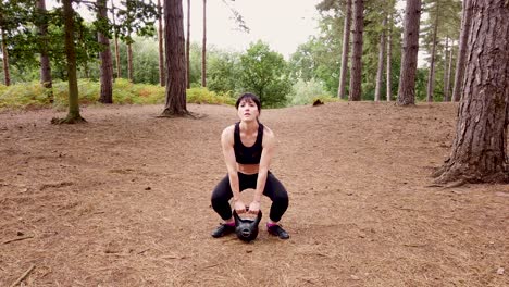 Girl-working-out-with-a-kettle-bell-in-the-woods