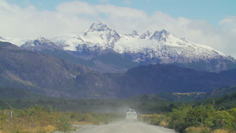 A-white-van-drives-down-a-gravel-road-head-toward-a-mountain-range