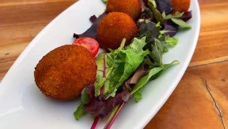 Traditional-Spanish-croquettes-with-iberian-ham,-tasty-and-crispy-breaded-starter-dish-with-salad-in-a-restaurant,-tapas-in-Ibiza-Spain,-4K-shot