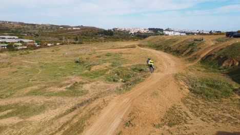 Luftaufnahme-Einer-Motocross-Strecke-In-Malaga,-Spanien,-Mit-Trockener,-Staubiger-Strecke-Und-Hügel,-Während-Ein-Motocross-Fahrer-Einen-Stunt-über-Einen-Hügel-Ausführt