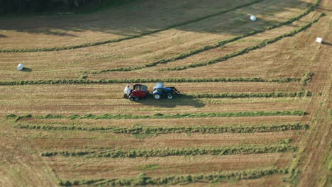 The-tractor-moving-slowly,-harvesting-grass-and-packaging-it-into-neat-white-plastic-rolls