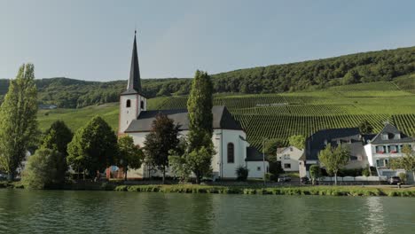 Scenic-view-of-a-church-at-a-river-bank-with-vineyards-in-the-background