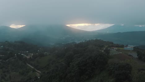 Flying-over-beautiful-green-mountains-during-a-cloudy-sunset-with-God-rays-in-Guatemala---Drone-aerial-tilt-up-shot