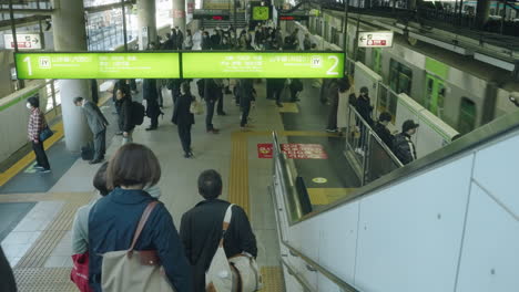 Menschen,-Die-Eine-Maske-Auf-Dem-Bahnsteig-In-Der-Yamanote-Linienstation-In-Tokio-Tragen,-Während-Der-Zug-Vorbeifährt---Hoher-Winkel,-Zeitlupe