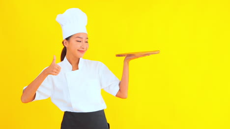Asiatische-Frau-Mit-Kochmütze,-Die-Ein-Schneidebrett-Aus-Holz-Hält