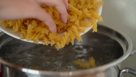 Female-hand-throwing-tortiglioni-pasta-into-boiled-water