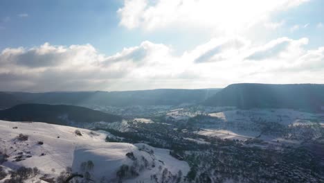 Aerial-flying-sideways-over-winter-wonderland-alongside-mountains-and-sun-reflecting-in-camera-overlooking-stunning-landscape-in-Swabia,-Germany