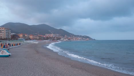 Panorama-of-Varazze-beach-at-sunset-with-all-its-typical-closed-umbrellas,-no-people-and-very-cloudy-sky-from-a-thunderstorm