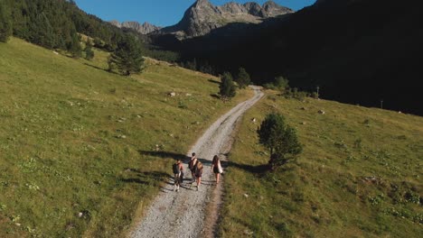Aerial-drone-shot-of-friends-walking-down-a-road-into-the-shadows-of-a-huge-mountain