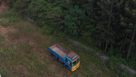 Aerial-view-over-a-colored-truck-parked-near-a-rainforest-jungle-in-a-greenery-natural-environment,-wide-shot,-conservation-concept