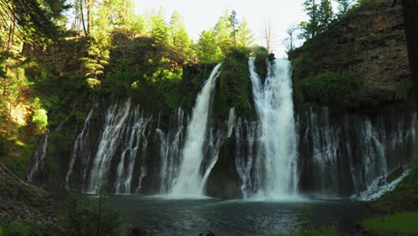 Panning-shot-of-Burney-Falls,-waterfall-in-California,-with-water-falling-down-a-cliff